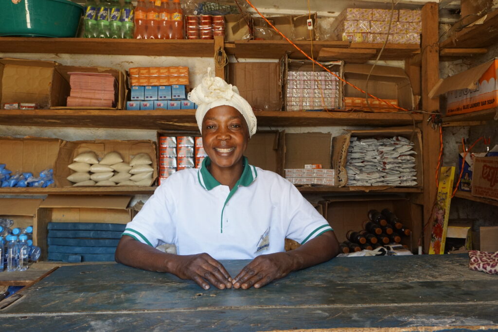 A smiling woman leaning on her arms in front of shelves with items to sell.