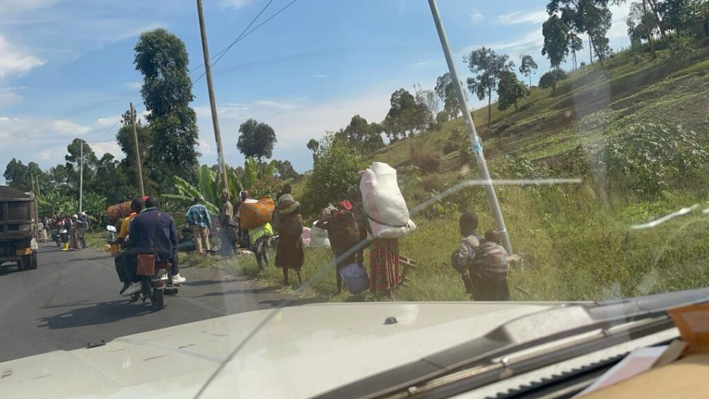 seen from a car, families with bundles of belongings walk alongside the road to flee their town