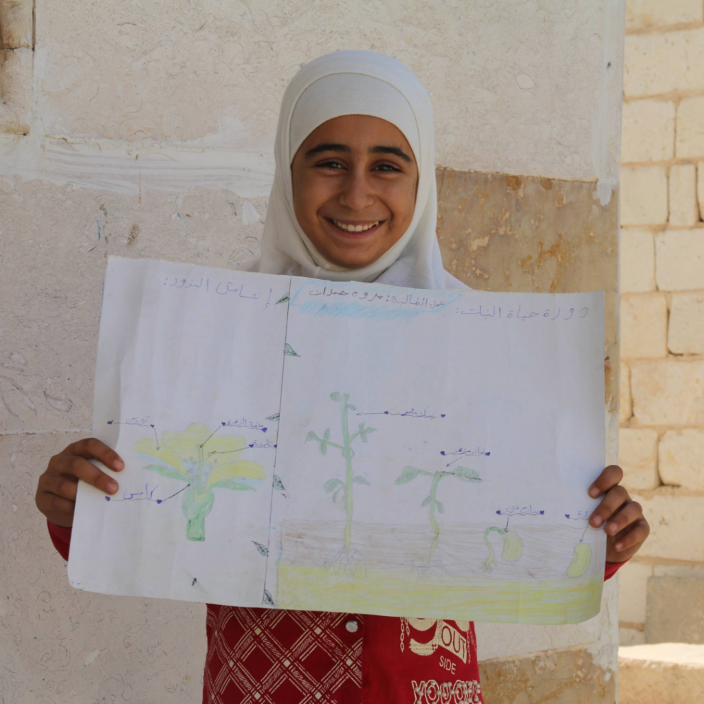A smiling girl holds up a hand-drawn poster of a tree, created during her biology class.