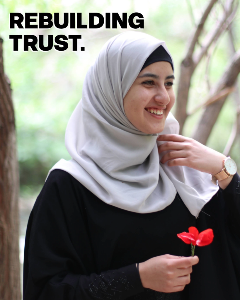A girl smiling into the distance holding a flower, quote reads 'rebuilding trust'