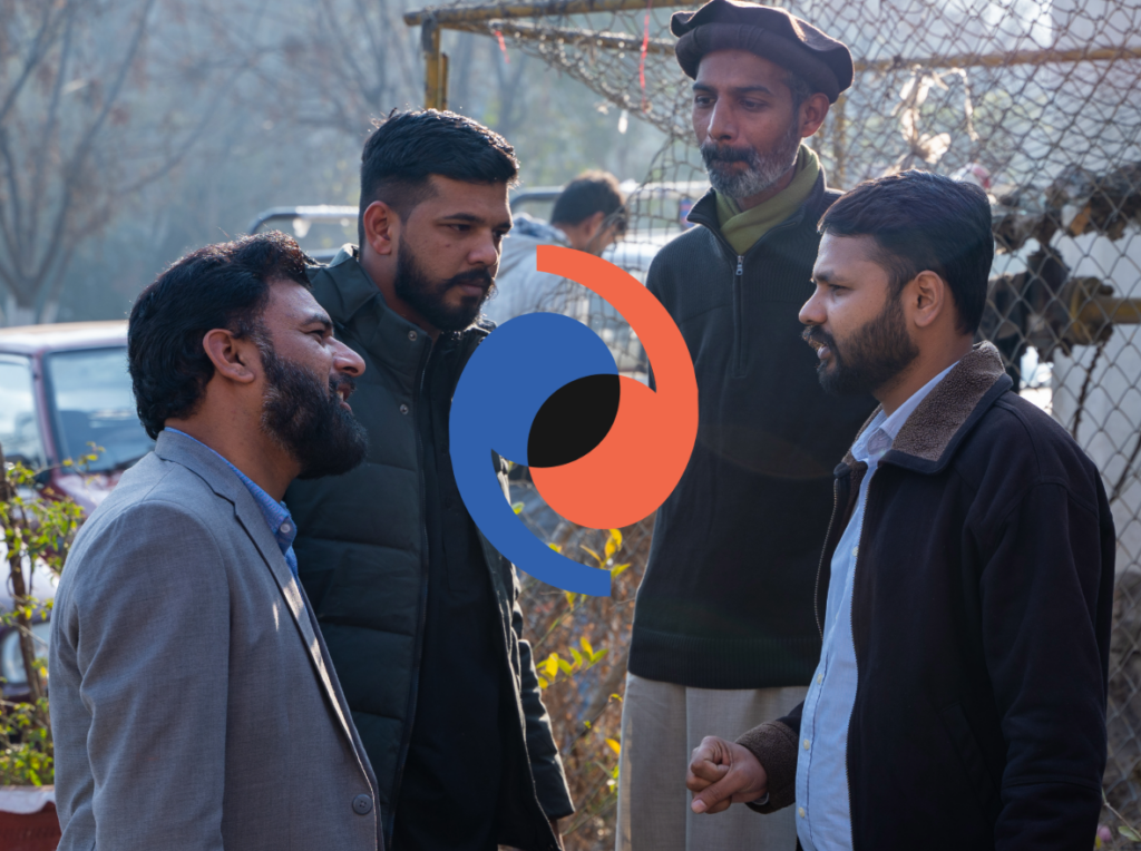A group of men talking in a circle outside. Blue and Red Peace Connect logo in centre